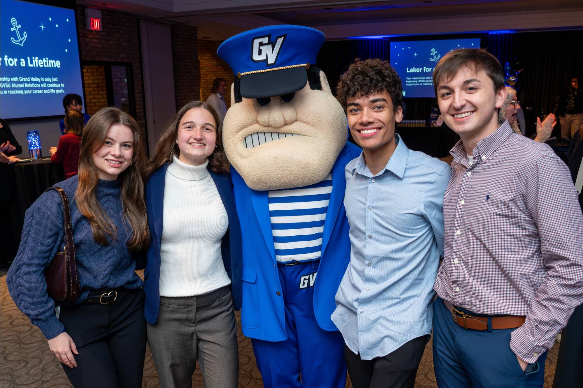 Four grads pose for a photo with Louie in a blue blazer